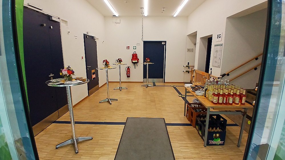 Der Eingang ins NIKOlino mit Stehtischen mit Blumen an der Seite und einem Buffet mit Getränken.