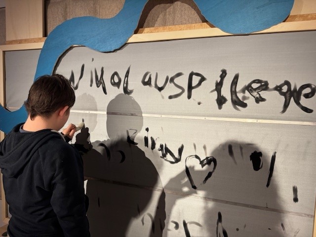 Ein Junge schreibt mit schwarzer Farbe auf eine weiße Wand Nikolauspflege